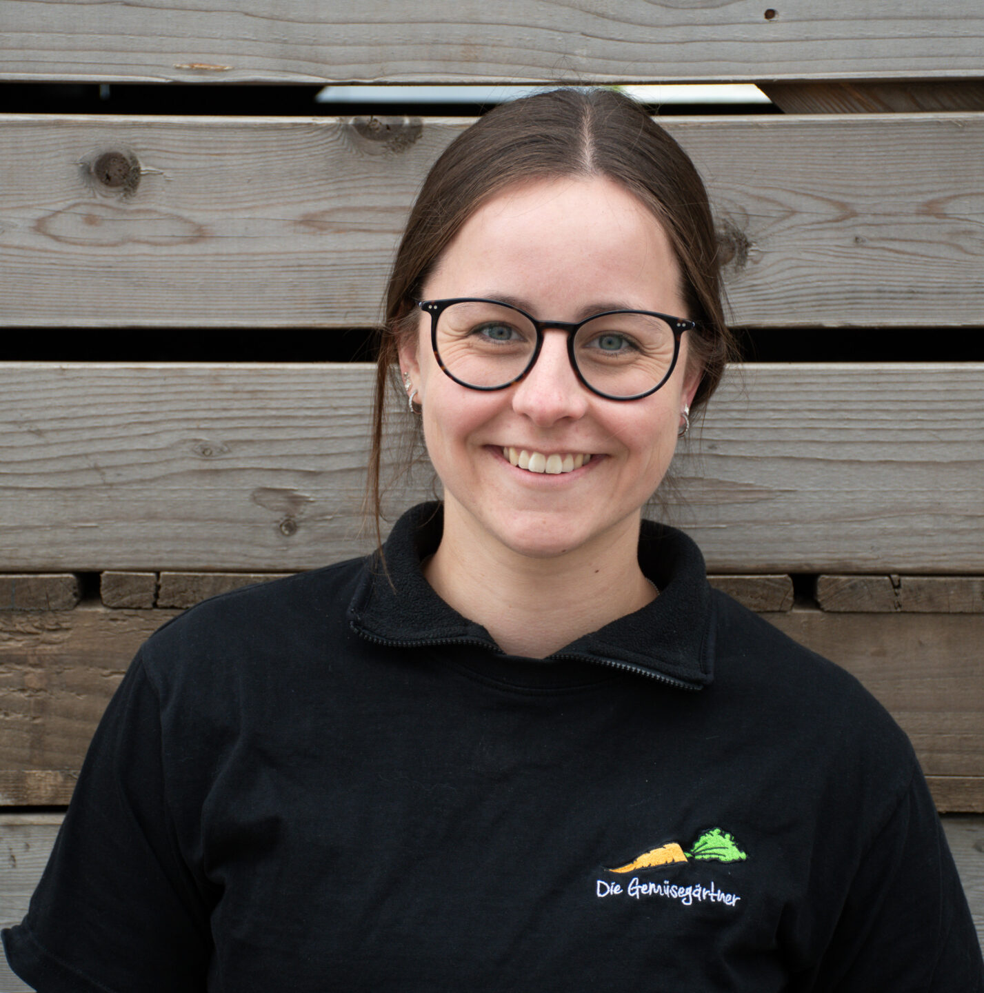 Junge braunhaarige Frau vor Holz mit Gemüsegärtner T-Shirt