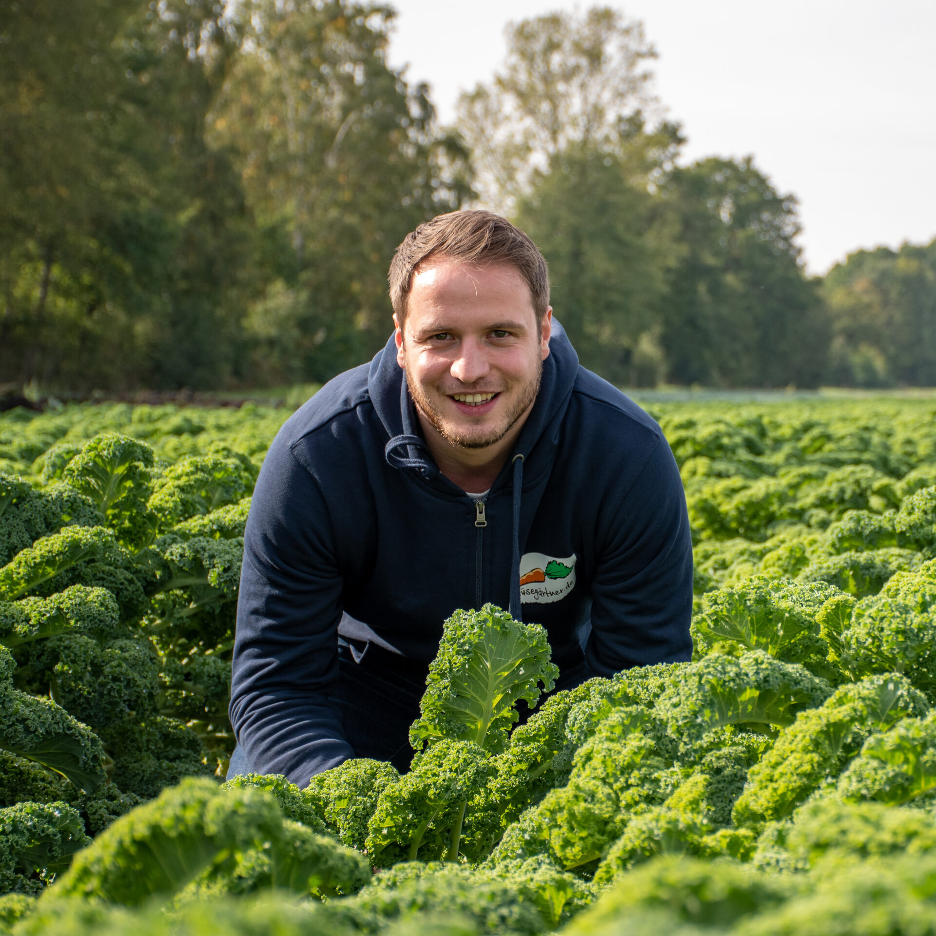 Rene steht lächelnd in einem Feld mit frischem Grünkohl .
