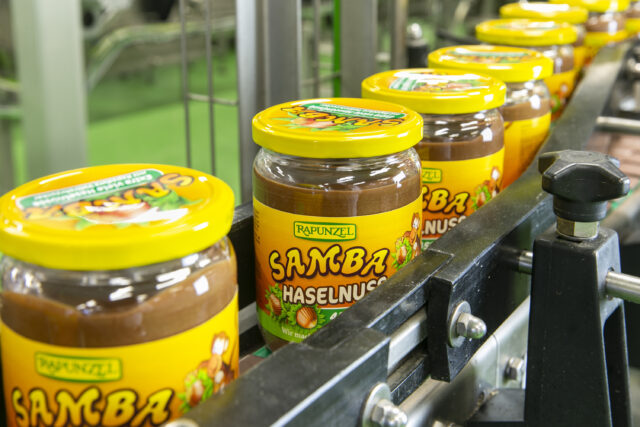 Gläser mit Rapunzel Samba Haselnusscreme fahren auf dem Förderband durch die Produktion.